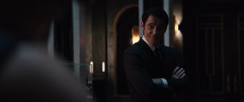 Movie still from “Hellraiser” (2022), directed by David Bruckner – A man wearing a suit and tie smiling for the camera; Medium shot, Over the shoulder angle