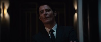 Movie still from “Hellraiser” (2022), directed by David Bruckner – A man wearing a suit and tie with his arms crossed; Close Up shot, Low angle