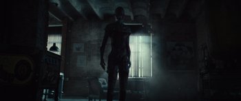 Movie still from “Hellraiser” (2022), directed by David Bruckner – A man standing in a dark room holding a cell phone; Wide shot, Low angle