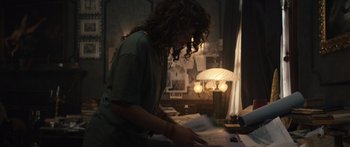 Movie still from “Hellraiser” (2022), directed by David Bruckner – A person sitting at a desk looking at papers; Medium shot, Over the shoulder angle