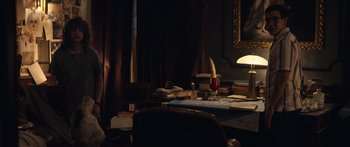 Movie still from “Hellraiser” (2022), directed by David Bruckner – A desk in a dark room with a lamp and books on the table; Wide shot, High angle