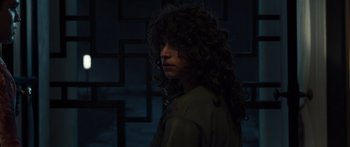 Movie still from “Hellraiser” (2022), directed by David Bruckner – A person with long curly hair standing in front of a wall; Close Up shot, Low angle
