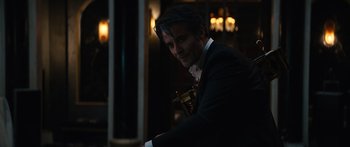 Movie still from “Hellraiser” (2022), directed by David Bruckner – A man in a suit and tie holding a gold cross; Medium shot, Over the shoulder angle