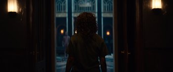 Movie still from “Hellraiser” (2022), directed by David Bruckner – A person with curly hair standing in front of a building at night; Wide shot, Over the shoulder angle
