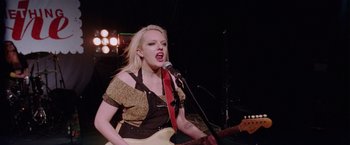 Movie still from “Her Smell” (2018), directed by Alex Ross Perry – A woman singing into a microphone while holding a guitar; Medium shot, Low angle