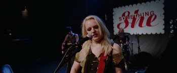 Movie still from “Her Smell” (2018), directed by Alex Ross Perry – A woman is singing into a microphone on a stage; Medium shot, Over the shoulder angle