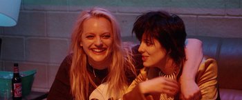 Movie still from “Her Smell” (2018), directed by Alex Ross Perry – Two young women smiling for the camera while sitting next to each other; Medium shot, Over the shoulder angle