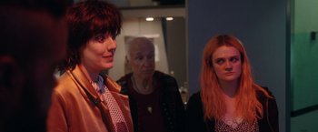 Movie still from “Her Smell” (2018), directed by Alex Ross Perry – A group of people standing next to each other in a room; Medium shot, Over the shoulder angle