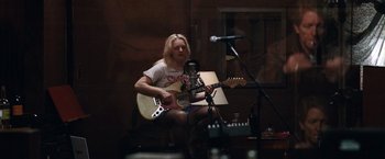 Movie still from “Her Smell” (2018), directed by Alex Ross Perry – A person sitting on a chair playing a guitar; Medium shot, High angle