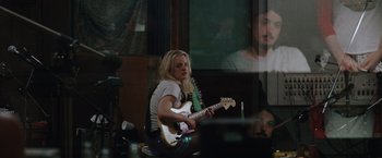 Movie still from “Her Smell” (2018), directed by Alex Ross Perry – A woman sitting in front of a microphone holding a guitar; Medium shot, Over the shoulder angle