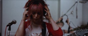 Movie still from “Her Smell” (2018), directed by Alex Ross Perry – A woman with pink hair is listening to headphones; Close Up shot, Over the shoulder angle