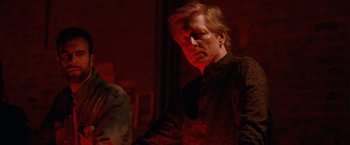 Movie still from “Her Smell” (2018), directed by Alex Ross Perry – A man in a black shirt is standing in a dark room; Medium shot, Over the shoulder angle