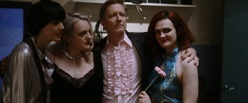 Movie still from “Her Smell” (2018), directed by Alex Ross Perry – A man in a suit with two other women; Medium shot, Low angle