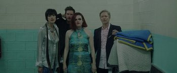 Movie still from “Her Smell” (2018), directed by Alex Ross Perry – A group of people standing next to each other in a room; Medium shot, High angle