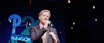 Movie still from “Her Smell” (2018), directed by Alex Ross Perry – A man holding a microphone while standing on a stage; Close Up shot, Over the shoulder angle