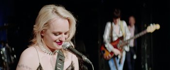 Movie still from “Her Smell” (2018), directed by Alex Ross Perry – A woman holding a microphone while a man plays a guitar; Close Up shot, Over the shoulder angle