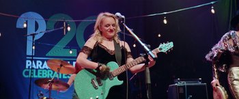 Movie still from “Her Smell” (2018), directed by Alex Ross Perry – A woman in a black dress is playing a guitar; Medium shot, Low angle