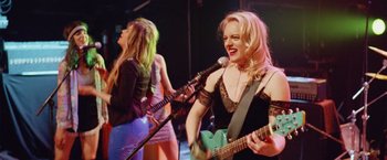 Movie still from “Her Smell” (2018), directed by Alex Ross Perry – Two women are performing on a stage with guitars; Medium shot, Low angle