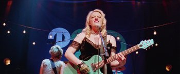 Movie still from “Her Smell” (2018), directed by Alex Ross Perry – A woman in a black dress is playing a guitar; Medium shot, Low angle