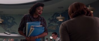 Movie still from “Hidden Figures” (2016), directed by Theodore Melfi – A woman holding a stack of papers in a room; Medium shot, Over the shoulder angle