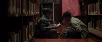 Movie still from “Hidden Figures” (2016), directed by Theodore Melfi – Two young boys sitting on the floor reading a book; Medium shot, High angle