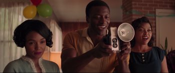 Movie still from “Hidden Figures” (2016), directed by Theodore Melfi – A man holding a camera and smiling at the camera; Medium shot, Low angle