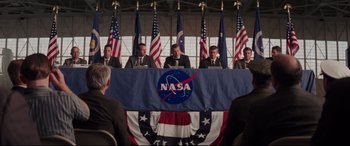 Movie still from “Hidden Figures” (2016), directed by Theodore Melfi – A group of men sitting at a table in front of a nasa sign; Wide shot, Low angle