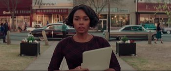 Movie still from “Hidden Figures” (2016), directed by Theodore Melfi – A woman holding a laptop while standing on the sidewalk; Medium shot, Low angle
