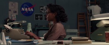 Movie still from “Hidden Figures” (2016), directed by Theodore Melfi – A person sitting at a table with a book in front of them; Medium shot, Over the shoulder angle