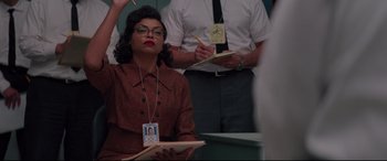 Movie still from “Hidden Figures” (2016), directed by Theodore Melfi – A woman in a brown dress holding a notebook; Medium shot, Over the shoulder angle