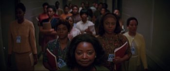 Movie still from “Hidden Figures” (2016), directed by Theodore Melfi – A group of people standing in a room with papers; Medium shot, High angle