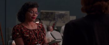 Movie still from “Hidden Figures” (2016), directed by Theodore Melfi – A woman in a red and black dress is holding a microphone; Medium shot, Over the shoulder angle