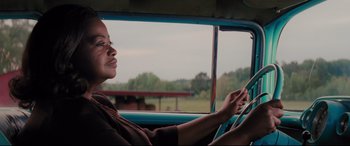Movie still from “Hidden Figures” (2016), directed by Theodore Melfi – A woman sitting in the driver's seat of a car looking at her cell phone; Medium shot, Over the shoulder angle