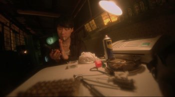 Movie still from “Fallen Angels” (1995), directed by Kar-Wai Wong – A man sitting at a table with a cigarette in his mouth; Close Up shot, Overhead angle