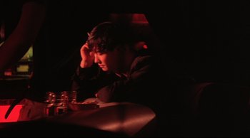 Movie still from “Fallen Angels” (1995), directed by Kar-Wai Wong – A man sitting at a table in a dimly - lit room; Medium shot, High angle