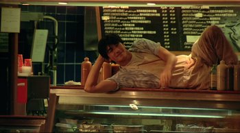 Movie still from “Fallen Angels” (1995), directed by Kar-Wai Wong – A man sitting on a counter in front of a display case; Medium shot, High angle