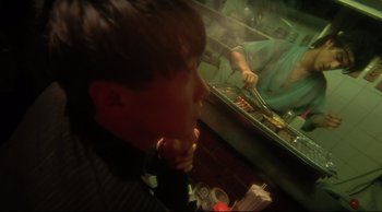 Movie still from “Fallen Angels” (1995), directed by Kar-Wai Wong – A man sitting in front of a counter with food on it; Medium shot, Over the shoulder angle