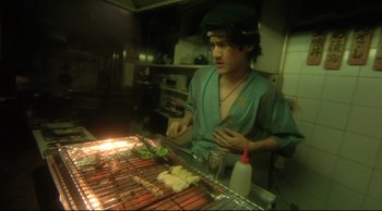 Movie still from “Fallen Angels” (1995), directed by Kar-Wai Wong – A man cooking food on top of an open grill; Medium shot, High angle