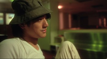 Movie still from “Fallen Angels” (1995), directed by Kar-Wai Wong – A young man wearing a hat and sitting in a room; Close Up shot, Low angle