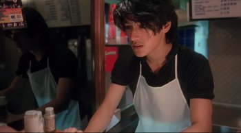 Movie still from “Fallen Angels” (1995), directed by Kar-Wai Wong – A young man wearing an apron and a black shirt is sitting at a counter; Medium shot, Low angle