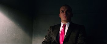 Movie still from “Hitman: Agent 47” (2015), directed by Aleksander Bach – A man wearing a suit and tie in front of a wall; Close Up shot, Low angle