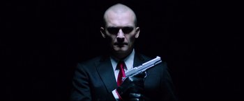 Movie still from “Hitman: Agent 47” (2015), directed by Aleksander Bach – A man in a suit and tie holding a gun; Close Up shot, Low angle