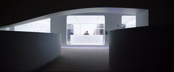 Movie still from “Hitman: Agent 47” (2015), directed by Aleksander Bach – A man sitting at a desk in a room; Wide shot, Low angle