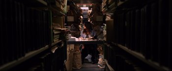 Movie still from “Hitman: Agent 47” (2015), directed by Aleksander Bach – A woman sitting at a desk in a room full of papers; Wide shot, High angle