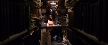 Movie still from “Hitman: Agent 47” (2015), directed by Aleksander Bach – A woman sitting at a desk in a room full of books; Wide shot, High angle
