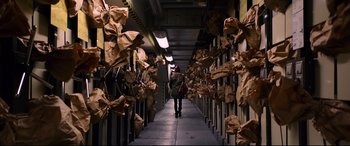 Movie still from “Hitman: Agent 47” (2015), directed by Aleksander Bach – A woman walking down a hallway lined with brown paper bags; Wide shot, Overhead angle