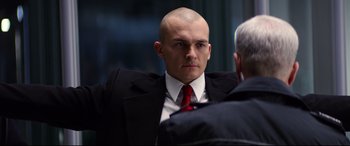 Movie still from “Hitman: Agent 47” (2015), directed by Aleksander Bach – A man in a suit and red neck tie; Close Up shot, Over the shoulder angle