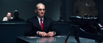 Movie still from “Hitman: Agent 47” (2015), directed by Aleksander Bach – A man sitting at a table in front of a camera; Medium shot, Low angle
