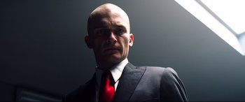 Movie still from “Hitman: Agent 47” (2015), directed by Aleksander Bach – A man in a suit and red neck tie; Close Up shot, Low angle