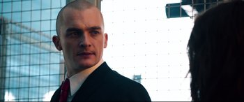 Movie still from “Hitman: Agent 47” (2015), directed by Aleksander Bach – A man in a suit and tie standing in front of a window; Close Up shot, Low angle